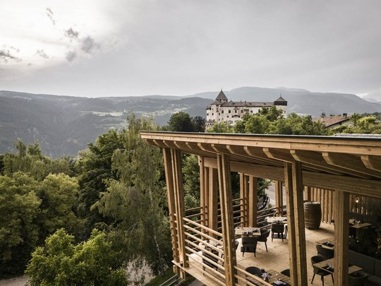 Presulis: Ihre Luxus-Ferienwohnung in Völs am Schlern Holzterrasse mit Tischen und Blick auf ein Schloss und bewaldete Berge