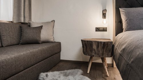 Presulis: Ihre Luxus-Ferienwohnung in Völs am Schlern Gemütliche Ecke mit grauem Sofa, Holztisch und Bett im Schlafzimmer
