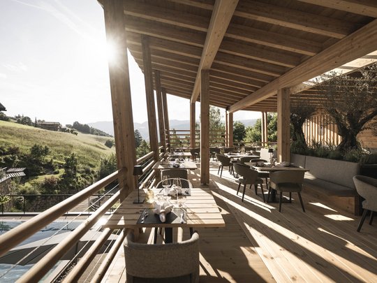 Presulis: Ihre Luxus-Ferienwohnung in Völs am Schlern Holzüberdachte Terrasse mit gedeckten Tischen und Blick auf grüne Hügel