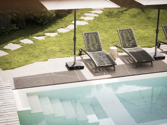 Presulis: Ihre Luxus-Ferienwohnung in Völs am Schlern Leere Liegestühle mit Sonnenschirmen neben einem Swimmingpool im Garten