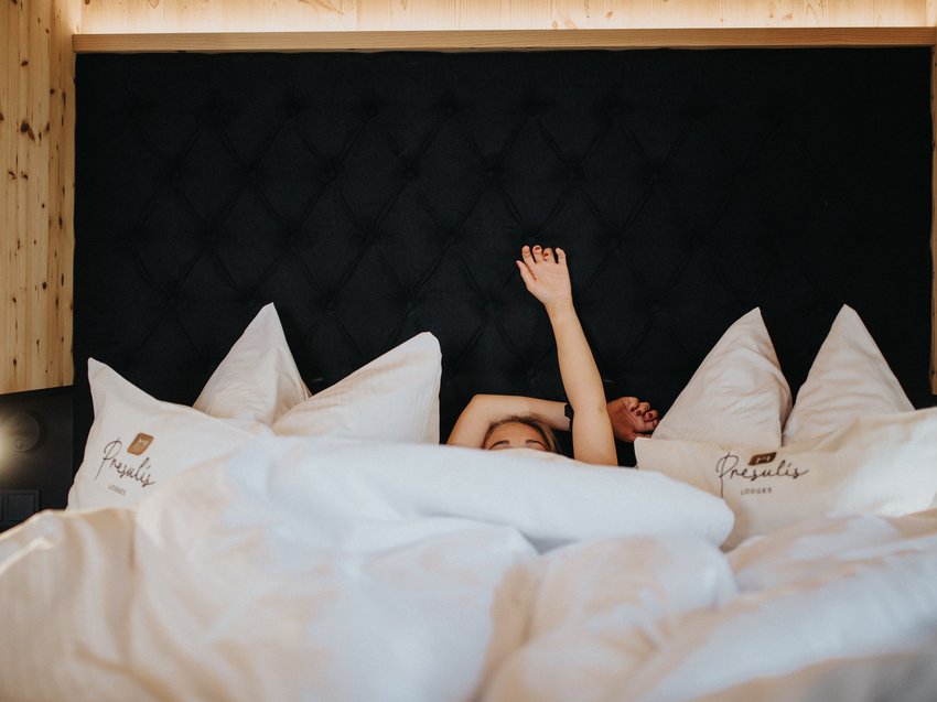 Presulis: Dein Adults-only-Hotel in den Dolomiten Person liegt im Bett mit weißen Kissen und hebt einen Arm nach oben